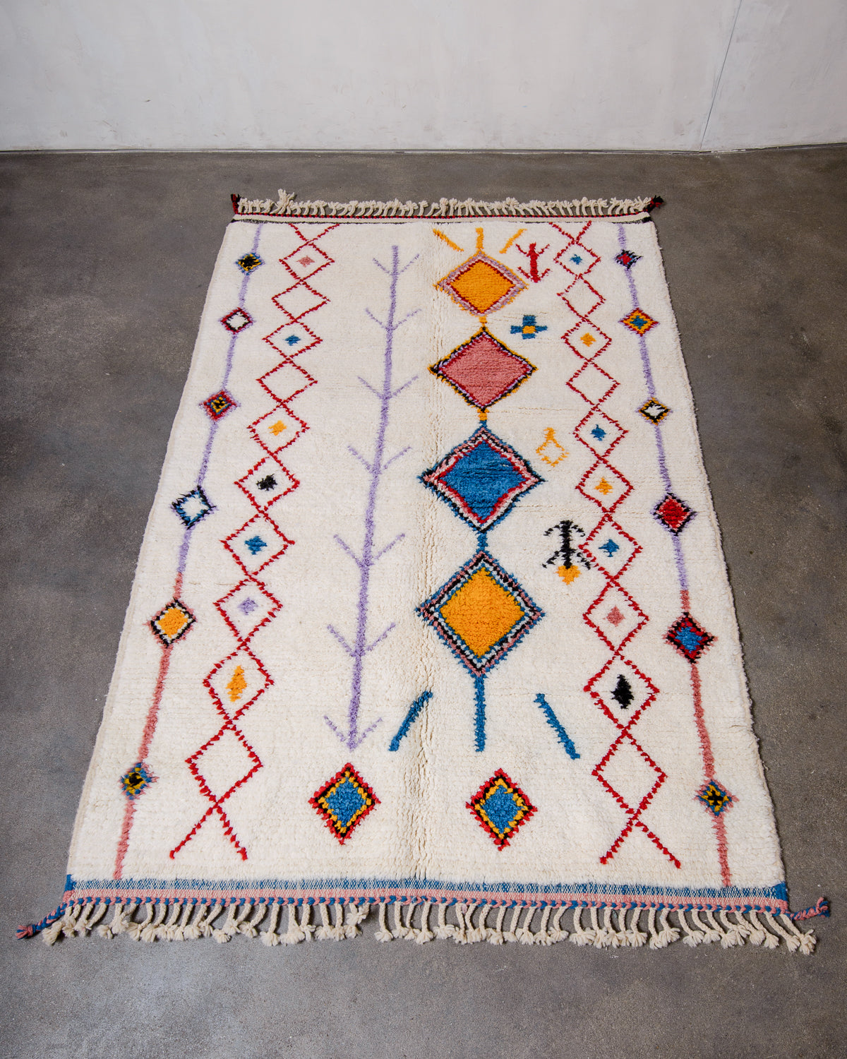 Berberlin Beniourain rug in cream wool with colourful motifs, laying flat on concrete studio floor.